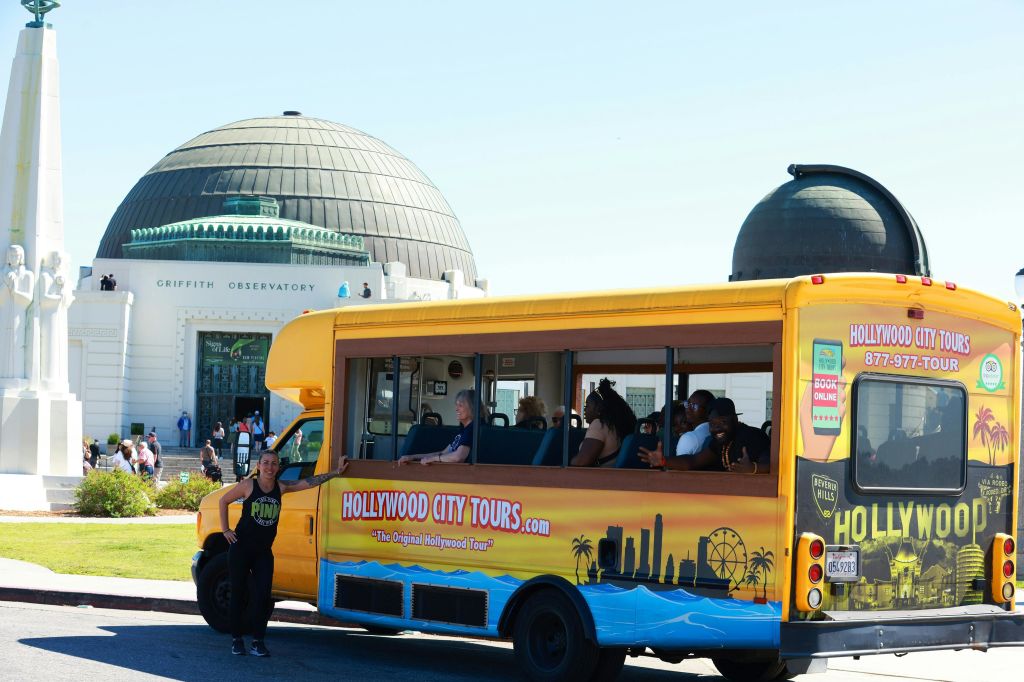 그리피스 천문대 근처에 노란색 할리우드 시티 투어 버스가 주차되어 있고 관광객들이 내부에 있습니다. 버스 밖에 가이드가 서 있습니다.