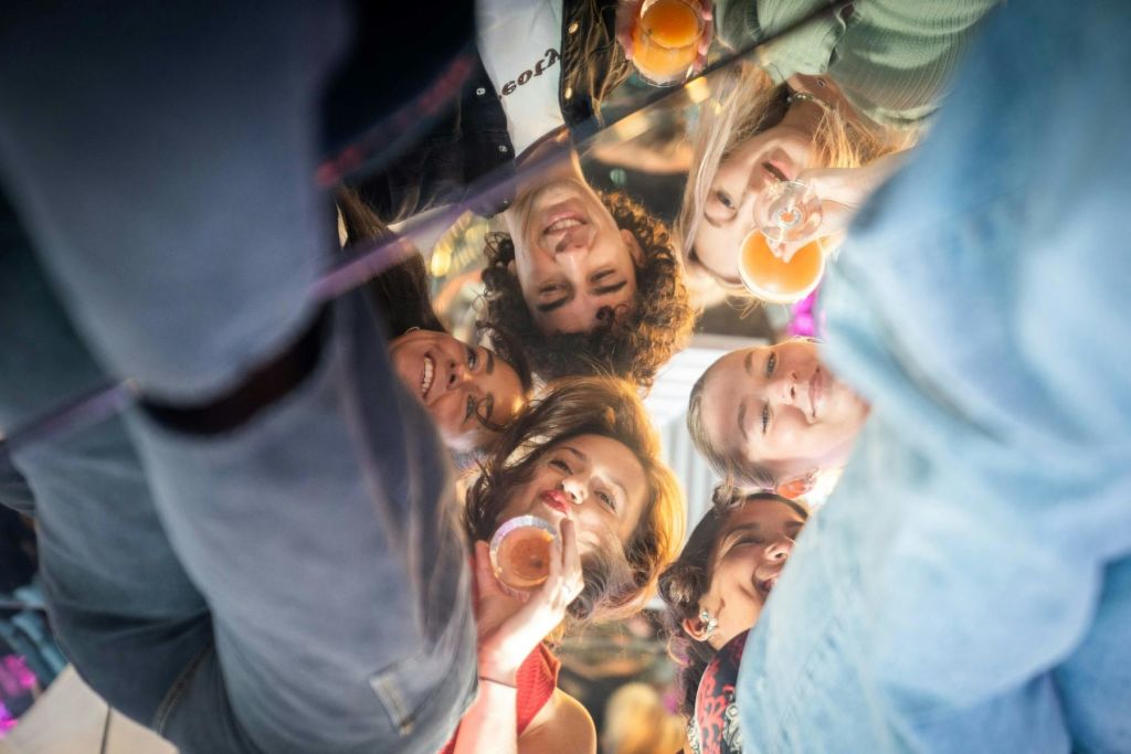 아래에서 바라본 6명의 친구들이 미소를 지으며 음료와 함께 잔을 들어 올리고 있습니다.