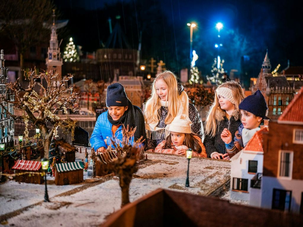 겨울옷을 입은 다섯 명의 어린이가 밤에는 조명이 켜진 미니어처 마을을 탐험합니다.