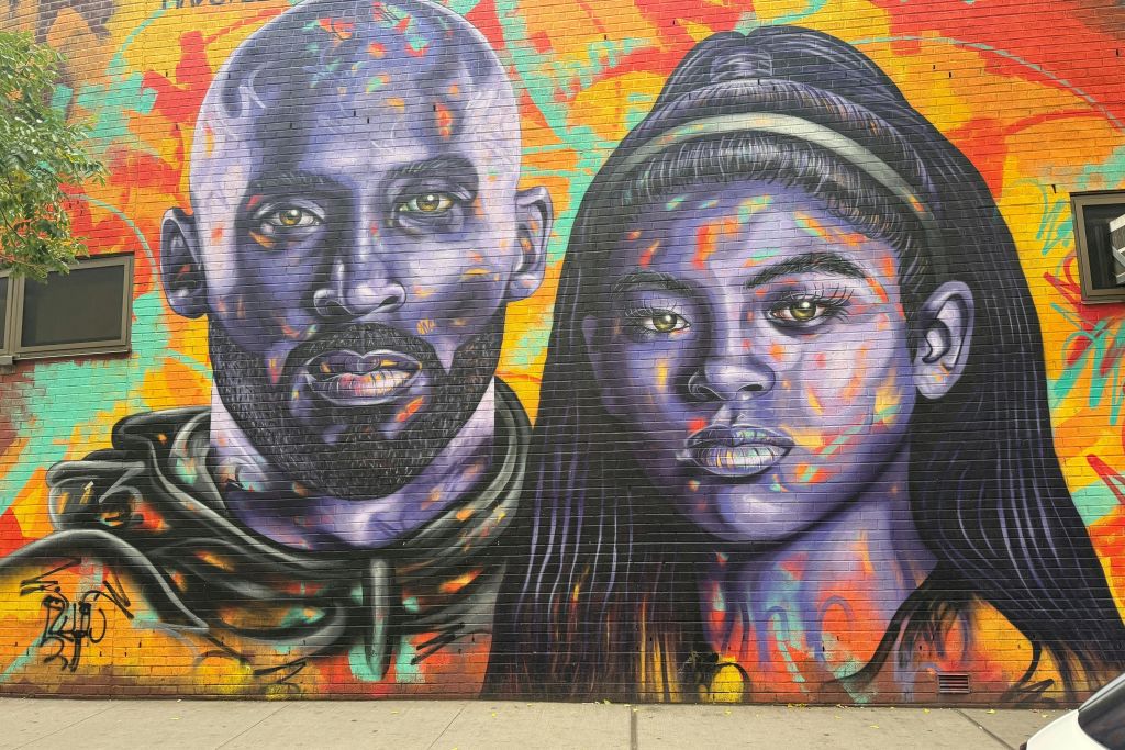 추상적이고 다양한 색상의 배경에 두 개의 생생하고 보라색 톤의 얼굴이 있는 벽돌 벽에 화려한 벽화가 있습니다.