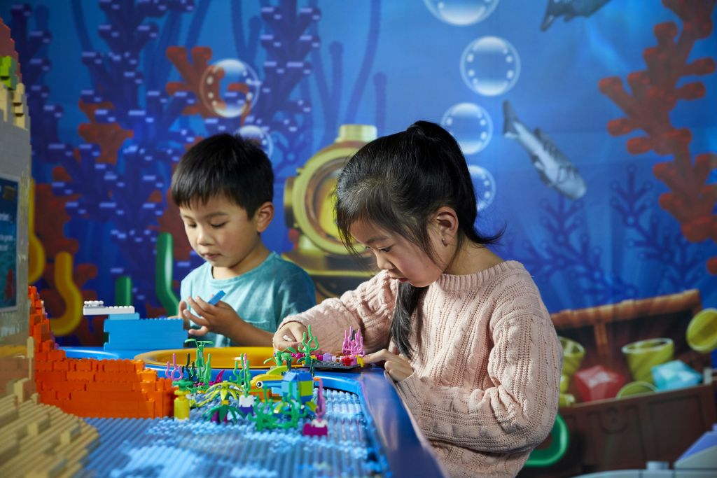 두 어린이는 다채로운 수중 테마 배경으로 둘러싸인 테이블에서 레고 작품을 만듭니다.
