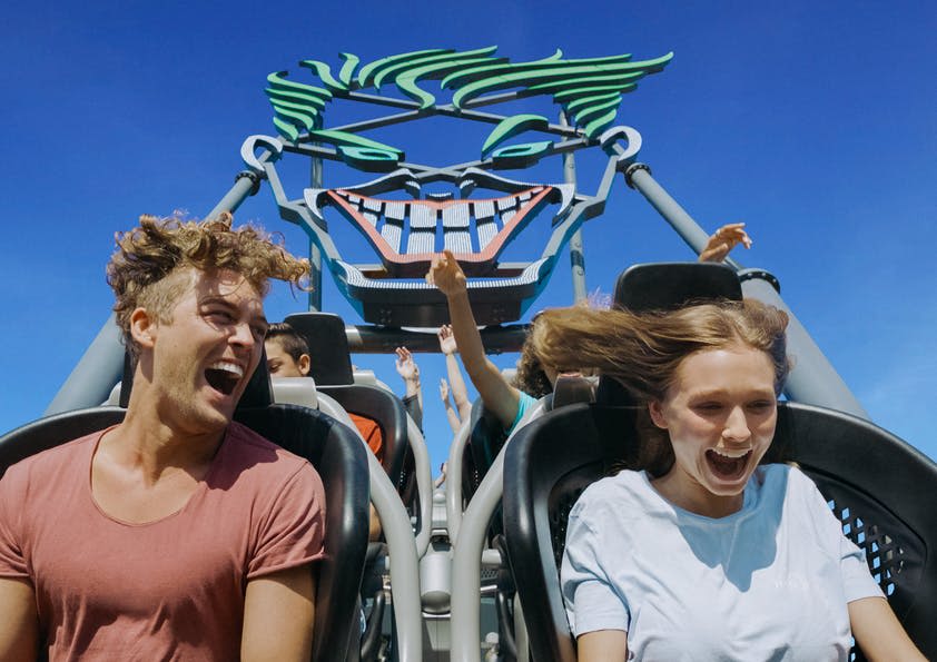 롤러코스터를 타며 팔을 들고 미소를 짓는 사람들, 만화 같은 얼굴 구조가 배경입니다.