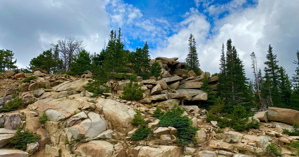 부분적으로 흐린 푸른 하늘 아래 상록수가 흩어져 있는 바위 언덕.