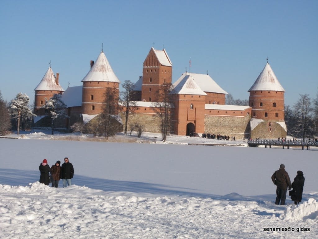 여러 개의 둥근 탑이 있는 커다란 벽돌 성 근처의 눈 속에 서 있는 사람들은 모두 맑고 푸른 하늘 아래 눈으로 덮여 있습니다.