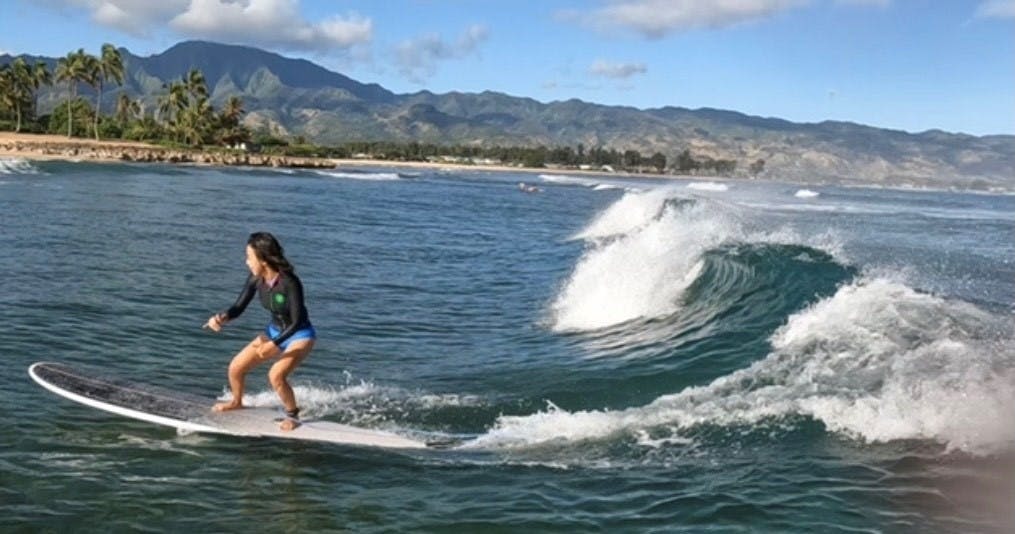산이 우거진 해안선과 맑고 푸른 하늘을 배경으로 파도를 타고 서핑하는 사람.