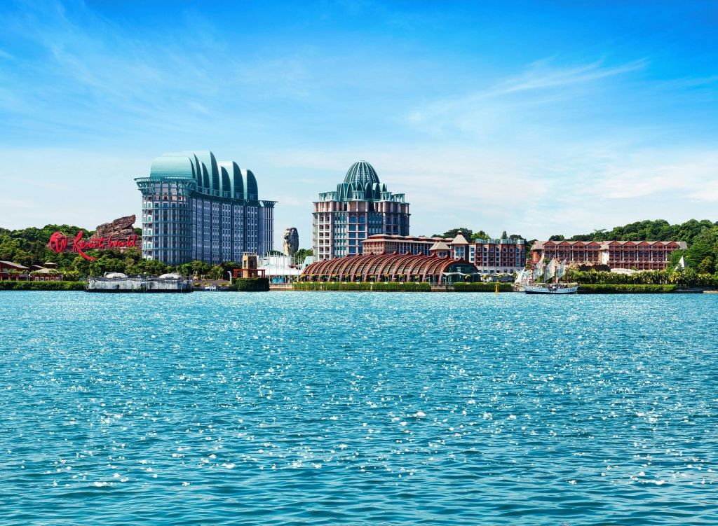 독특한 돔형 지붕과 수변이 있는 건물은 푸른 하늘과 맞닿아 있으며, 전경에 반짝이는 물이 흐르고 있습니다.