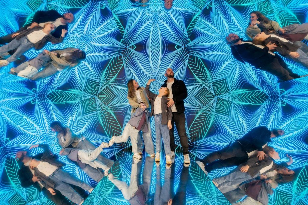 다채로운 만화경 패턴 앞에 세 사람이 반사 표면에 서서 거울처럼 반사됩니다.