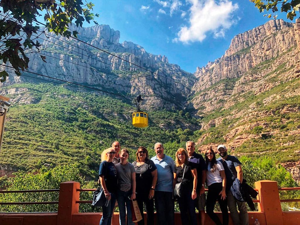 노란색 케이블카를 배경으로 산악 풍경 앞에서 포즈를 취하고 있는 한 무리의 사람들.