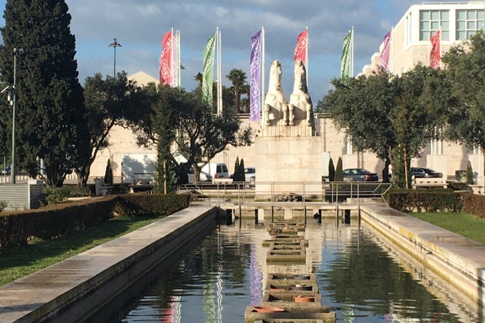화창한 날을 배경으로 반사되는 수영장, 깃발, 나무가 있는 돌 받침대 위에 놓인 두 마리의 말 동상.