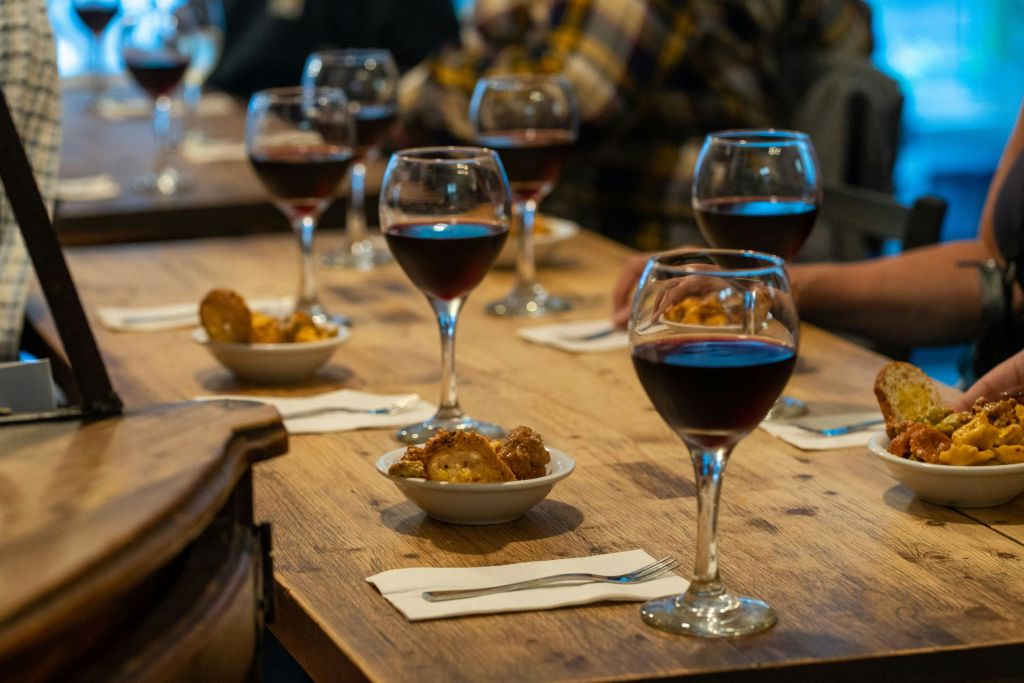 냅킨과 포크가 놓인 나무 테이블에 레드 와인 몇 잔과 애피타이저 작은 그릇이 놓여 있습니다.