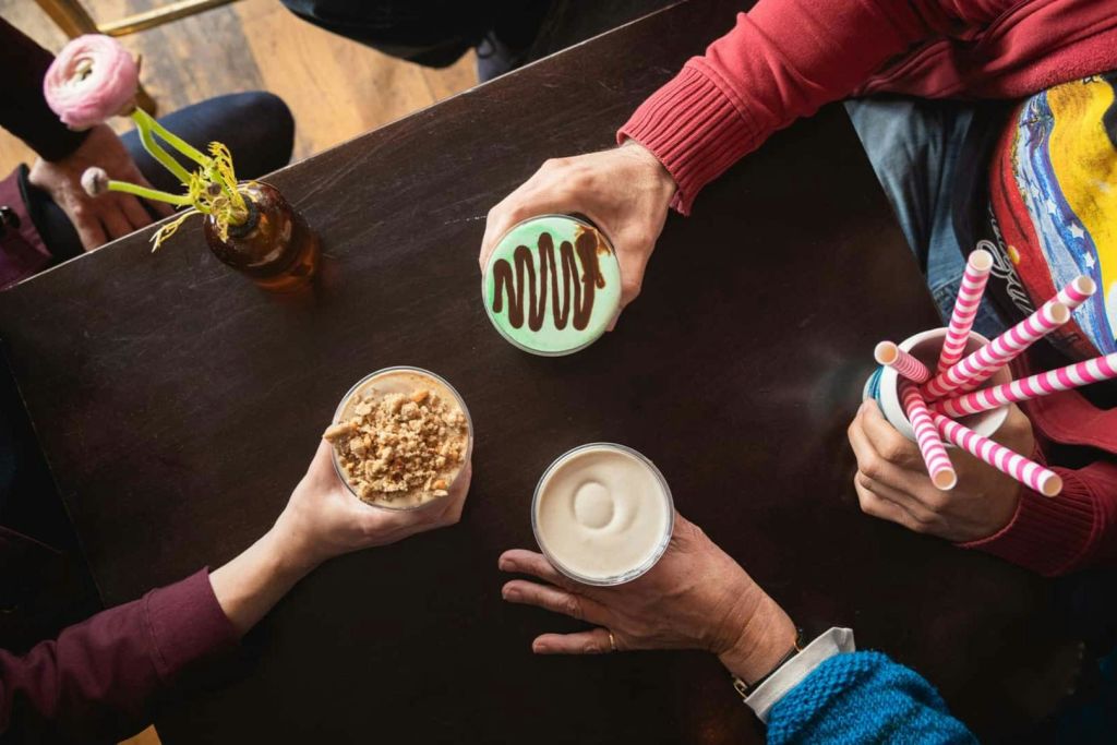 손만 보이는 나무 테이블에서 서로 다른 음료와 디저트를 들고 있는 세 사람.
