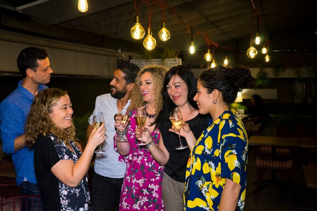 캐주얼한 실내 환경에서 매달린 조명 아래에서 와인잔을 들고 건배하는 사람들의 미소.