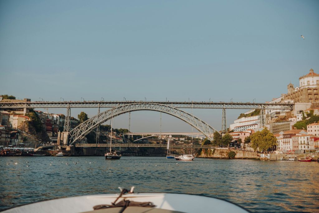 건물과 나무로 둘러싸인 커다란 아치형 다리를 배경으로 보트를 타고 강을 바라보는 풍경.