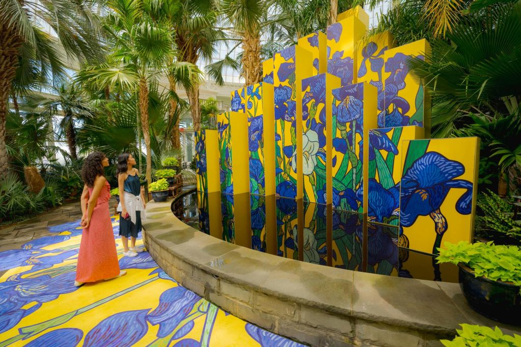 열대 실내 정원의 다채롭고 거울로 장식된 예술 작품 앞에 두 명의 여성이 서 있습니다.