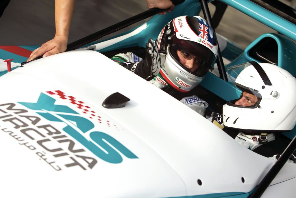 헬멧을 착용한 경주용 차량 운전자 두 명이 차량에 앉아 있으며, 한 명은 헬멧에 영국 국기를 달고 있습니다. 한 사람이 근처에 서 있습니다.