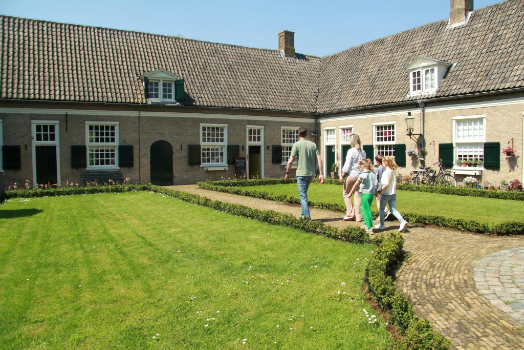 타일로 마감된 지붕이 있는 벽돌 건물로 둘러싸인 잘 정돈된 안뜰을 지나 4인 가족이 통로를 걷고 있습니다.