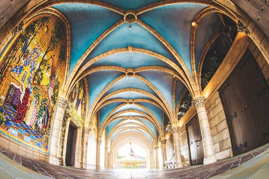 벽에 파란 천장과 석조 아치, 조명으로 장식된 모자이크 벽화가 있는 아치형 복도입니다.