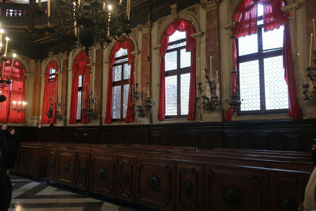 커다란 창문, 빨간색 커튼, 목재 페우, 천장에 걸린 화려한 샹들리에가 있는 웅장한 객실입니다.