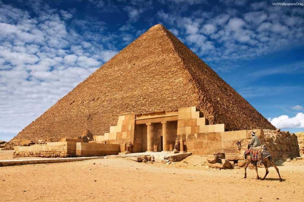 입구와 주변 모래 풍경이 보이는 부분적으로 흐린 하늘 아래 기자의 대피라미드.