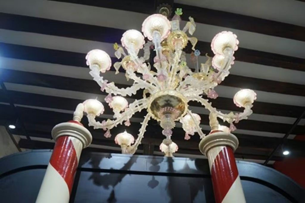 실내의 두 줄무늬 기둥 사이에 분홍색과 흰색 유리 디테일이 매달려 있는 장식용 샹들리에입니다.