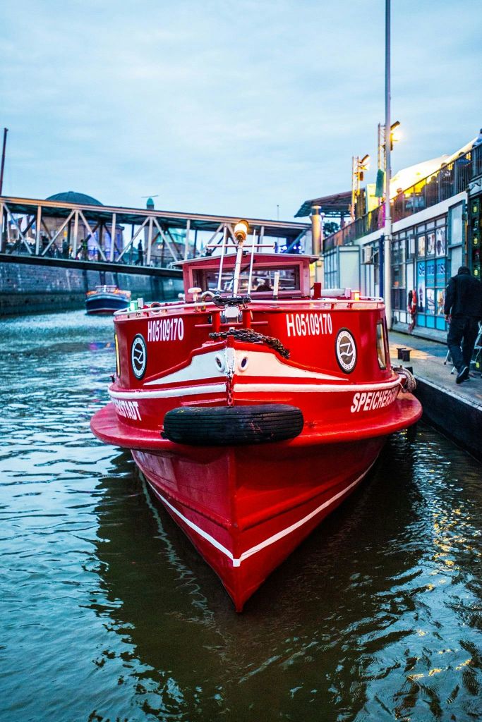 붉은 보트가 다리, 건물, 사람을 배경으로 운하에 정박하고 있습니다.