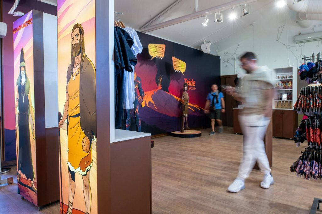 옷걸이와 기념품, 벽에 걸린 벽화, 흐릿한 두 사람이 지나가는 가게의 내부.