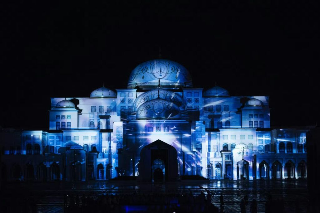 밤에는 돔과 아치가 있는 조명 건물로, 외관에 파란색과 흰색 투영 디스플레이가 있습니다.