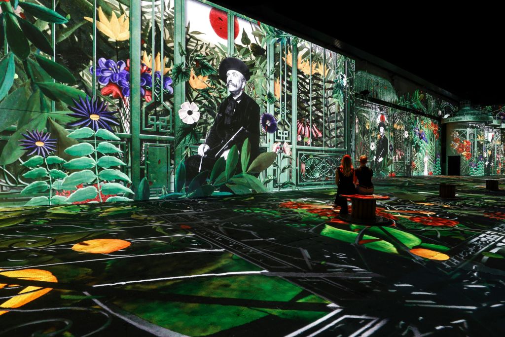 화려한 꽃과 한 남자의 흑백 초상이 돋보이는 생동감 넘치는 디지털 아트 디스플레이를 감상하는 두 사람.