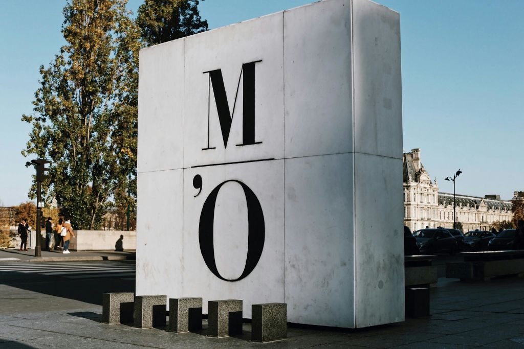 "M O" 문자가 있는 커다란 흰색 정육면체 구조. 나무와 건물의 일부를 배경으로 합니다.