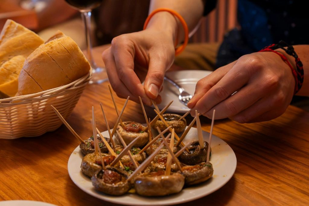 한 사람이 접시에 버섯을 넣고 빵과 와인 한 잔을 배경으로 이쑤시개를 놓습니다.