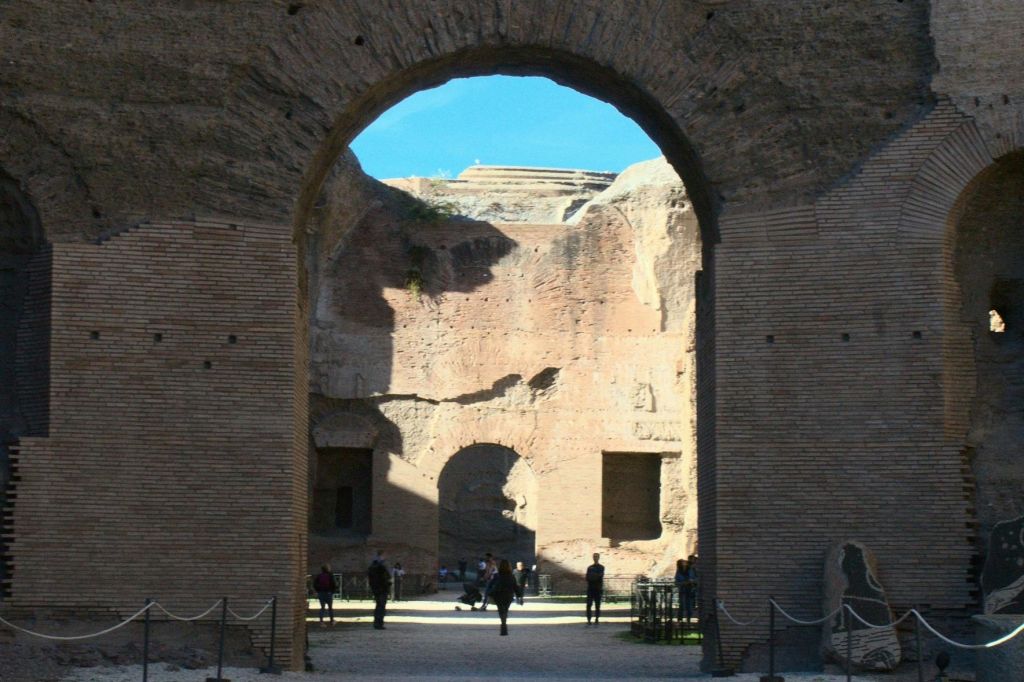 더 많은 아치, 걷는 사람들, 맑고 푸른 하늘이 있는 유적을 보여주는 고대 벽돌 아치형 통로입니다.