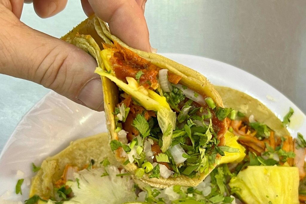 양념 돼지고기, 파인애플, 다진 양파, 고수로 채워진 갓 만든 타코 알 목사를 손에 들고.