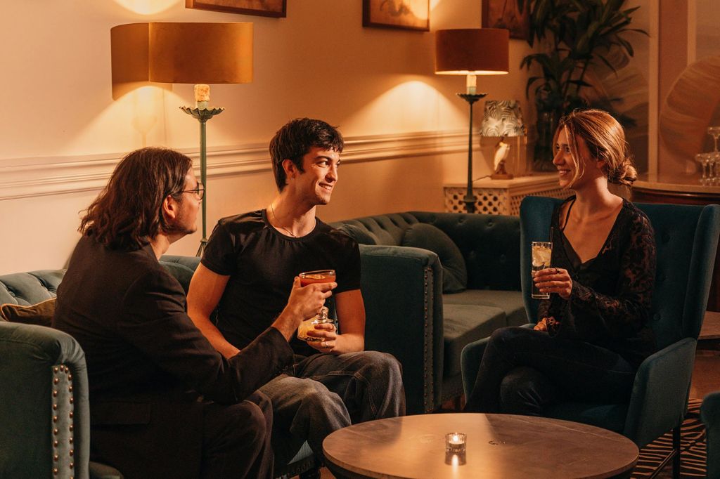 세 사람이 따뜻하게 불이 켜진 방의 소파에 앉아 음료를 마시며 대화를 나누고 있습니다.