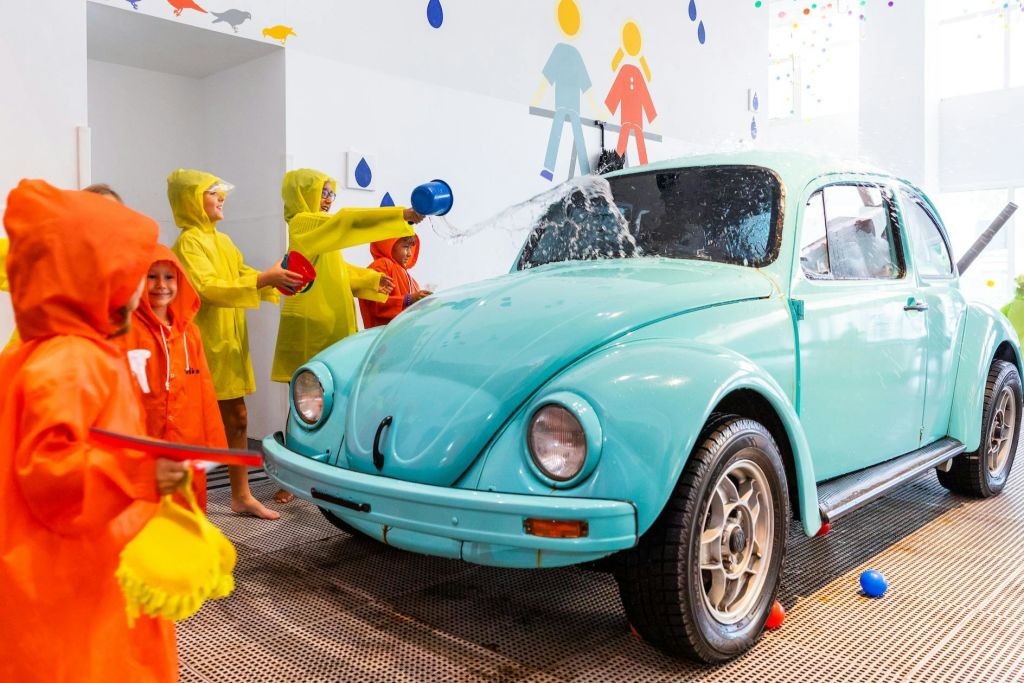 밝은 색상의 실내 환경에서 청록색 자동차, 튀는 물과 놀고 있는 비옷을 입은 어린이.
