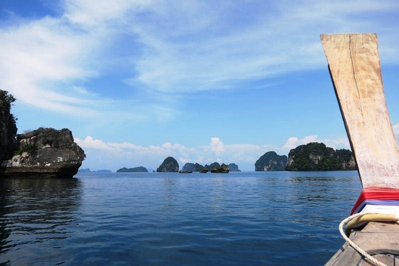 푸른 하늘 아래 먼 바위섬이 있는 잔잔한 바다, 오른쪽에 부분 보트가 보입니다.