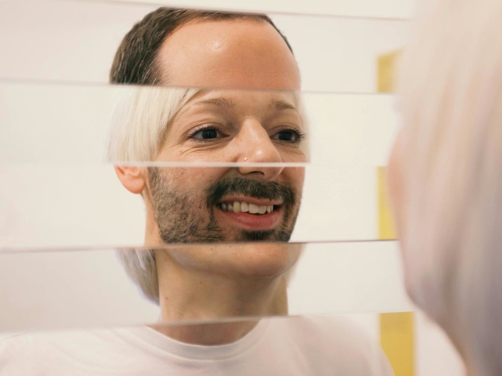 머리가 짧고 콧수염이 있는 사람은 조각난 거울을 들여다보며 반사가 조각난 것처럼 보입니다.