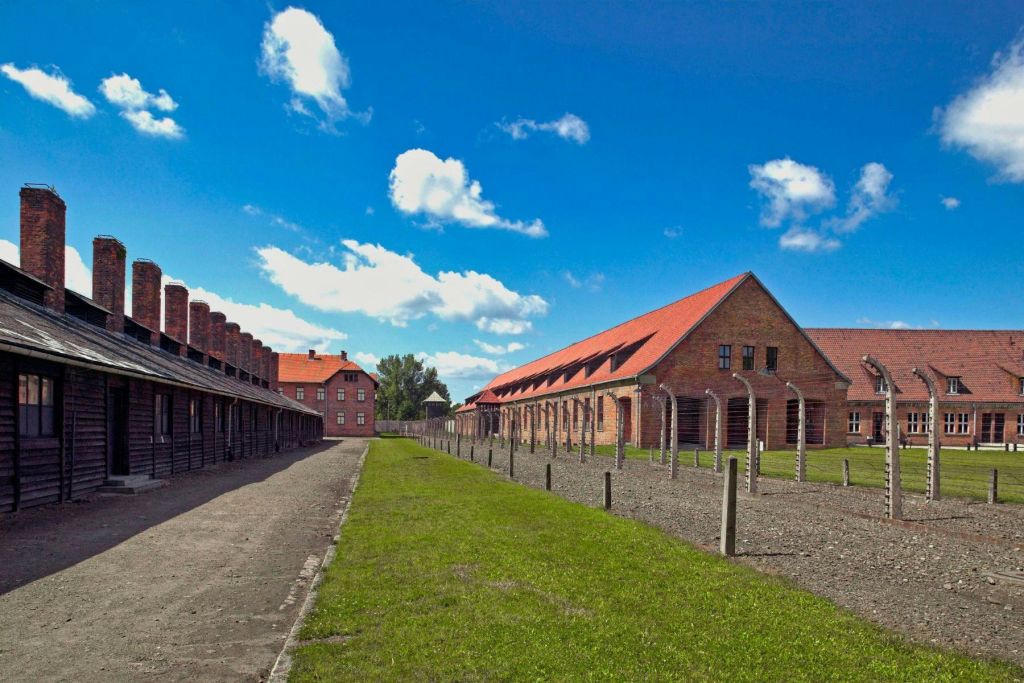 벽돌 건물, 붉은 기와 지붕, 구름 몇 개가 있는 맑고 푸른 하늘 아래 푸른 잔디밭이 있는 넓은 공간입니다.