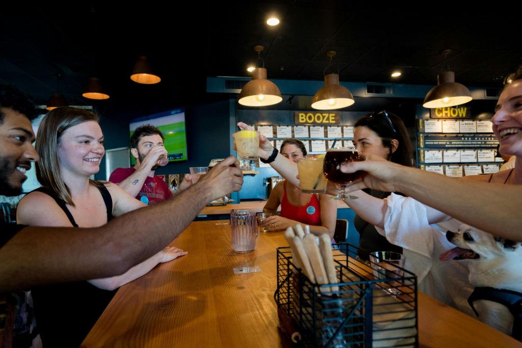 한 무리의 사람들이 바에 앉아 따뜻한 펜던트 조명 아래에서 건배를 하며 함께 음료를 마시고 있습니다.