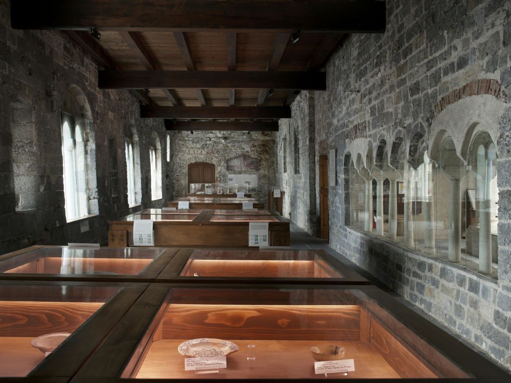 아치형 창문과 나무 천장이 있는 석조 벽으로 된 방으로, 유물을 전시한 나무 진열 케이스가 있습니다.