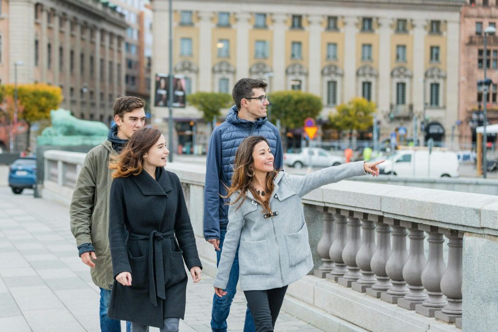 역사적인 건물과 거리를 배경으로 도시 보도를 걷고 미소를 짓는 네 명의 사람들.