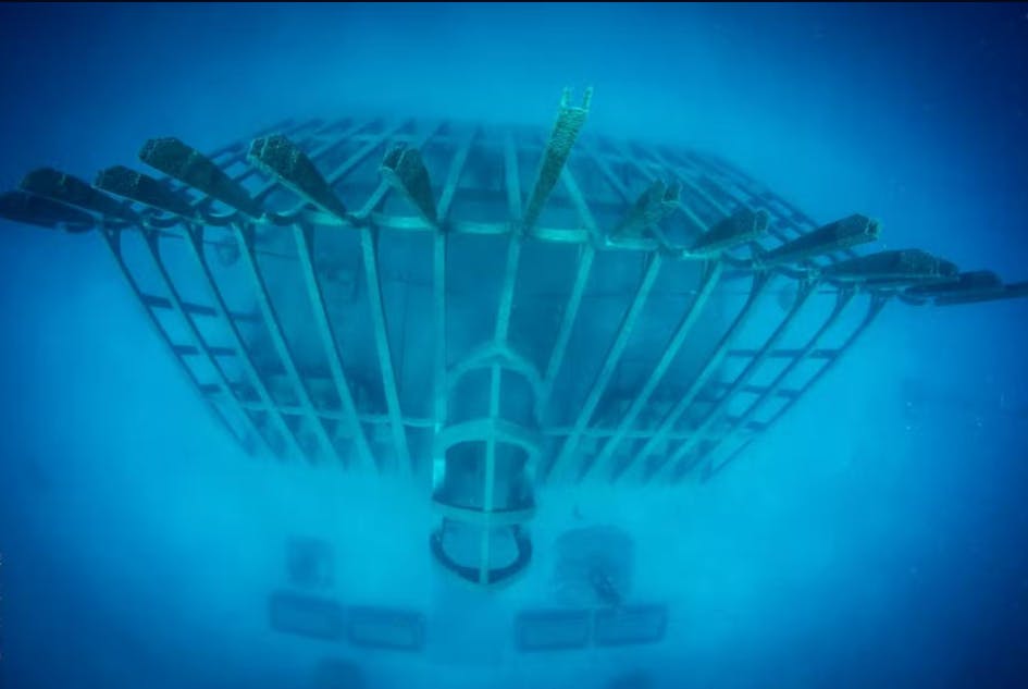 금속 격자 모양의 프레임워크와 푸른 수중 환경에서 아래에 보이는 물체가 있는 수중 구조물.