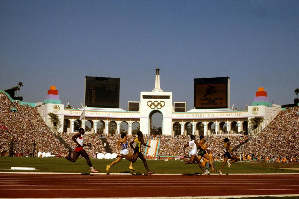 1984년 로스앤젤레스 올림픽에 출전하는 단거리 선수들은 경기장과 올림픽 링을 배경으로 경기를 펼칩니다.
