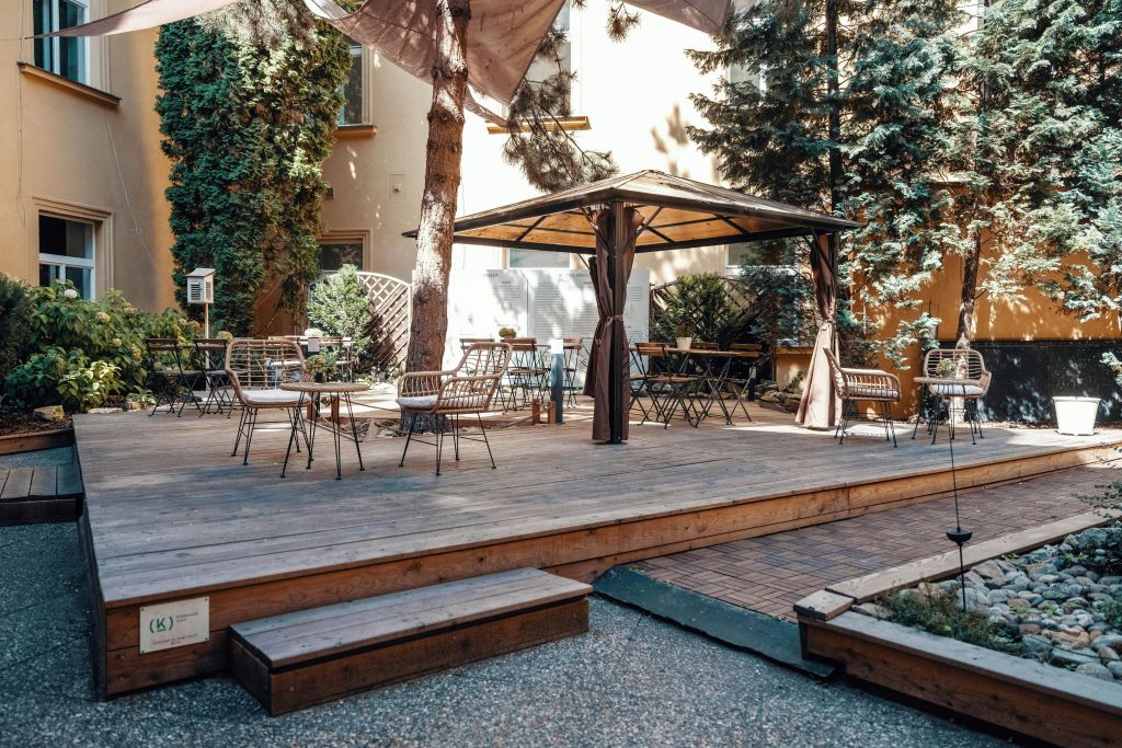 나무와 식물로 둘러싸인 캐노피로 그늘진 나무 데크, 빈 테이블과 의자가 있는 야외 파티오.