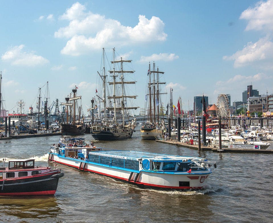 대형 선박, 길고 파란색과 흰색 선박, 수많은 선착장 범선 등 다양한 보트가 있는 바쁜 항구 풍경.