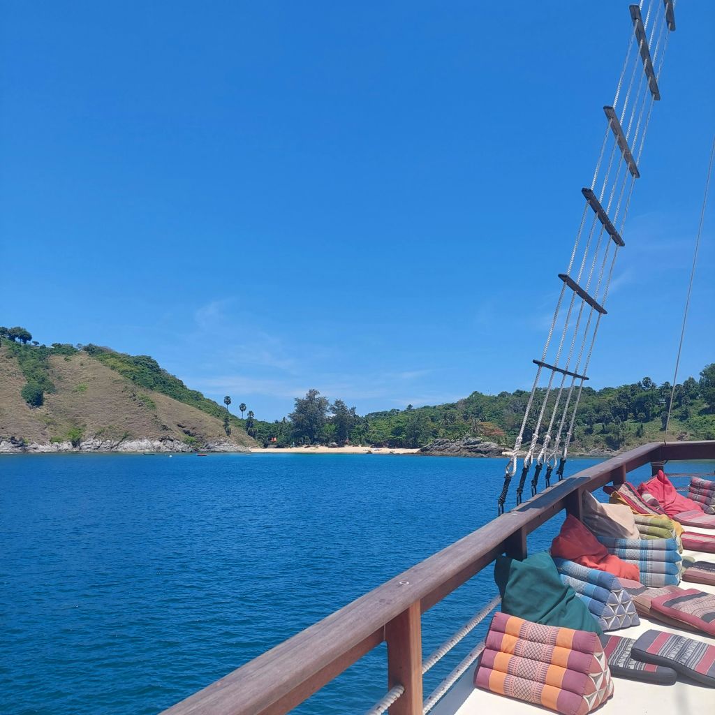 화려한 쿠션, 맑고 푸른 물, 밝고 푸른 하늘 아래 언덕이 많은 해안선이 있는 보트 데크.