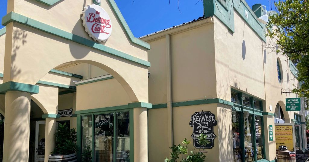 맑고 푸른 하늘 아래 'The Bottling Court' 와 'Key West's First Legal Rum Distillery' 표지판이 있는 건물.