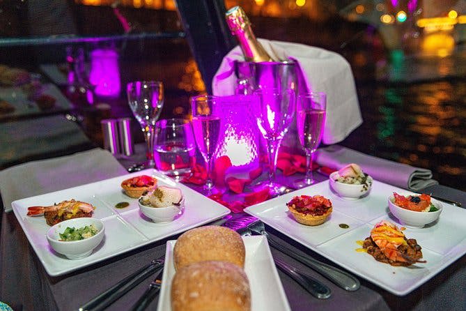 다양한 애피타이저, 빵 롤, 얼음 양동이에 담긴 샴페인, 보라색 무드 조명으로 장식된 유리잔이 놓인 테이블입니다.