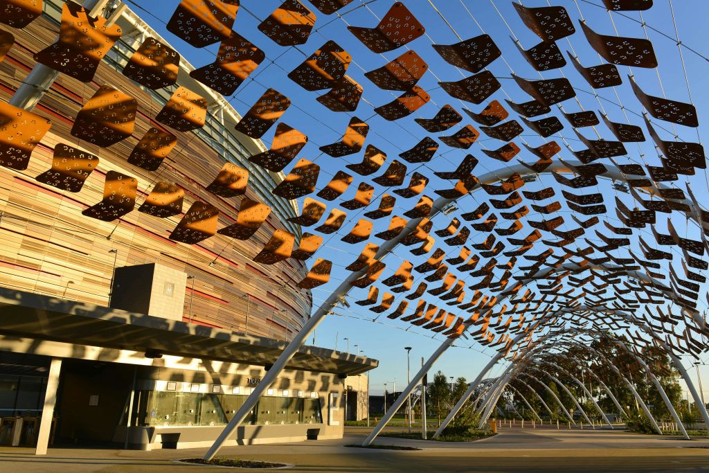유리창과 기둥이 있는 원형의 현대적인 건물 근처에 매달린 갈색과 검은색 패널이 있는 야외 설치물입니다.