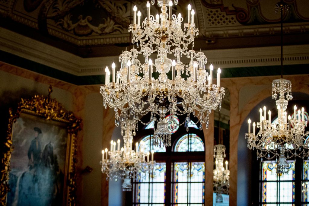 커다란 아치형 창문과 장식 천장이 있는 화려한 방에 조명 촛불이 달린 우아한 크리스탈 샹들리에.