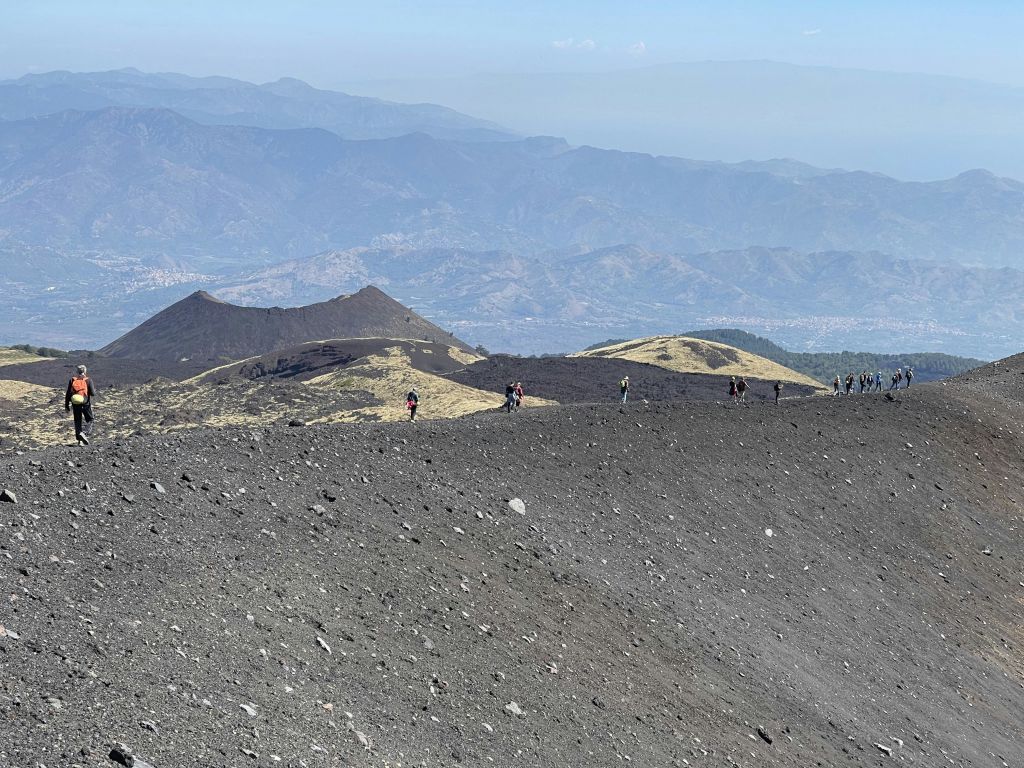 산맥과 흐릿한 하늘을 배경으로 바위투성이의 화산 지대에서 하이킹을 즐기는 사람들.